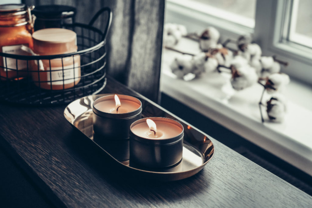 Burning candles on golden tray with cotton flowers in home interrior closeup